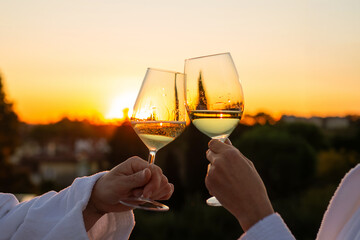 Couple toasts white wine sunset rooftop hotel bathrobe, romantic aperitif luxury celebration toast golden hour sunset romantic getaway