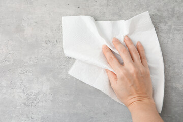 Woman wiping grey textured surface with paper towel, top view. Space for text