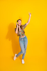 Young woman dancing with headphones against bright yellow background wearing floral top and jeans for lifestyle fashion and music vibe