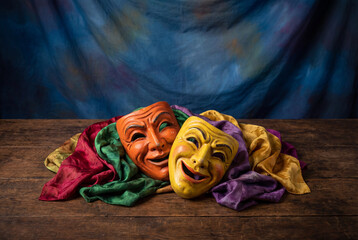 Comedy and tragedy theater masks on wooden table with colorful cloth
