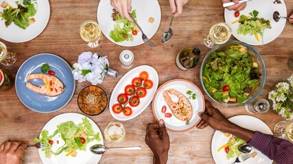 Top view of diverse hands enjoy lunch meal with salmon and salad, healthy food. Lunch menu, healthy salad and salmon on wood table, top view photo, diverse people hands enjoy lunch meal, sharing food
