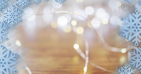 Twinkling fairy lights showing warm white bulbs over wooden tabletop, with blue snowflake cutouts