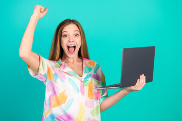 Young woman with raised hand and laptop expressing happiness on a turquoise background