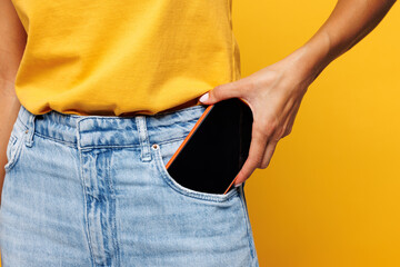 Close up cropped photo shot young woman int-shirt casual clothes hold put into pocket mobile cell phone with blank screen workspace area isolated on plain yellow orange background Lifestyle concept