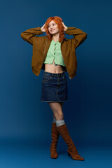 Young woman in stylish spring outfit with red hair poses gracefully against blue backdrop
