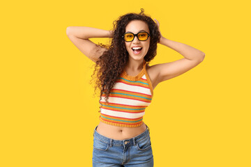 Beautiful African-American woman with sunglasses on yellow background