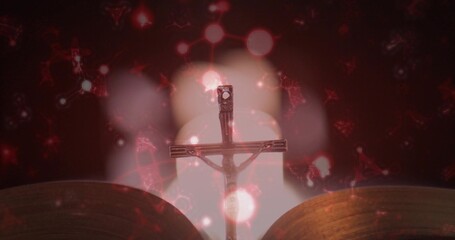 Silhouetting metal crucifix with corpus standing upright at altar, with open book and bokeh lights