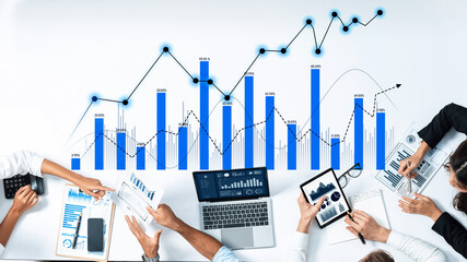 A diverse team engages in data analysis using laptops and digital devices while reviewing financial charts and graphs. The collaborative atmosphere promotes insights and strategies. Scalp