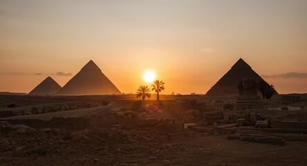 Warm sunset highlights Egyptian pyramids and Sphinx with palm tree shadows