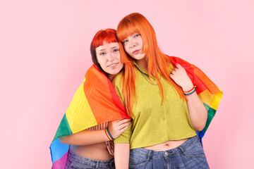 Lovely lesbian couple with rainbow flag on pink background. LGBT concept