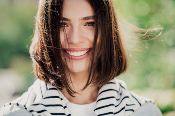 Smiling young woman portrait outdoors in natural light with short brown hair and striped sweater, happy casual lifestyle close-up showing bright smile and fresh spring atmosphere