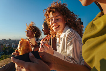 Diverse friends laughing eating pizza outdoors at sunset