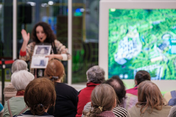 Group of older adults listening to presenter during guided tour, digital map screen in background, community education, social engagement, learning.