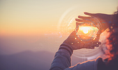 Hands framing the sun with futuristic digital hologram overlay at sunset. Future vision and technology concept.