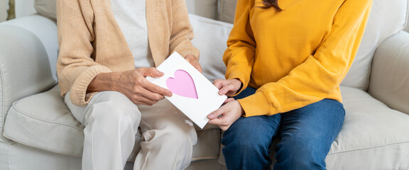 Happy mother's day.Happy asian daughter greeting mom with Mother's day and hugging her,sitting on dinner table at living room