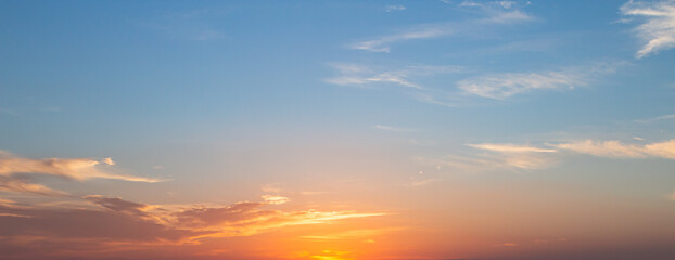Panoramic sunset sky background with vibrant orange and golden clouds under a soft blue twilight sky