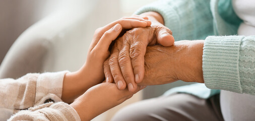 Senior woman with daughter holding hands at home, closeup