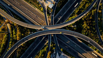 Aerial view capturing a complex motorway interchange, showing numerous roads and elevated highways intertwining with light traffic moving through the green urban infrastructure