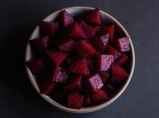 Bowl with diced cooked beets. Deep red vegetable pieces glistening with moisture on dark textured surface. Minimalist food presentation for healthy eating.