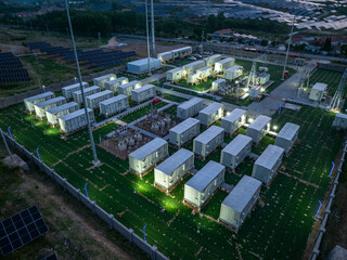 Aerial view of a large-scale energy storage power station operating at night with illuminated container modules and surrounding solar panels