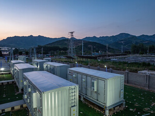 Energy storage power station with containerized equipment arrays located in mountainous terrain at dusk