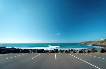 Empty asphalt parking area overlooks ocean waves crashing on rocky shore. Lighthouse stands on distant cliff under clear blue sky. Coastal landscape invites road trip travel.