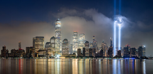 Dawn in Lower Manhattan with skyscrapers and low clouds and the September 11 Tribute in Light memorial lights. Financial District, New York City, USA