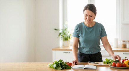 Woman planning a healthy diet with fresh vegetables in the kitchen. Female writing in a notebook for weight loss and nutrition