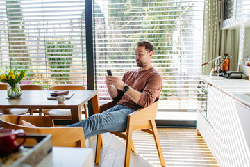 Man sitting in chair and browsing phone at home.