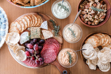 charcuterie board appetizers snacks food gourmet party platter with delicious salami cheese red grapes mixed nuts and assorted dips served on a rustic wooden dining table top.