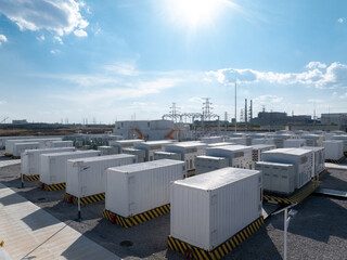 White containerized energy storage systems arranged in an outdoor power station facility