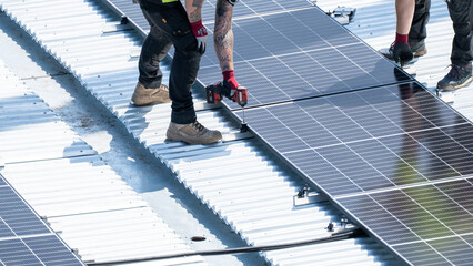 Multiple worker using drill to fasten solar panel row on bright rooftop