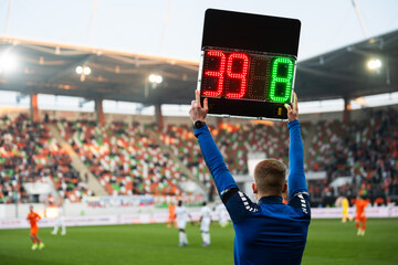 Rear view of a fourth official holding an electronic substitution board showing numbers 39 and 8 at a football stadium.