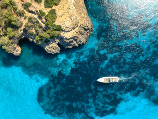 Aerial view of luxury motor boat yacht in turquoise sea water in Mallorca, Balearic island, Spain. Speedboat moving near rocky cliff coast. Drone summer landscape. Cruise. Top down view. Travel