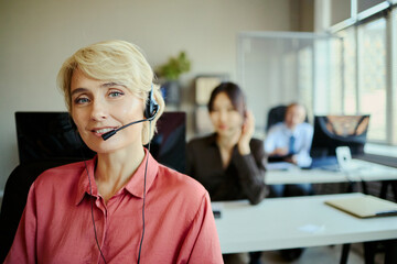 Portrait of smiling Caucasian young adult woman wearing headset and assisting customers in call center office, representing client support and team service for business marketing