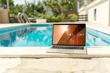 Laptop by the swimming pool displaying a forty-degree high temperature warning during a heatwave