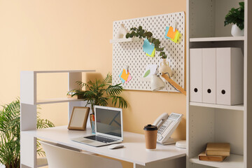 Interior of stylish office with workplace, pegboard and shelf unit