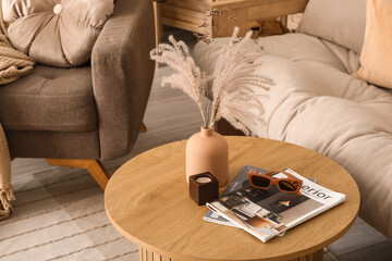 Vase with dry reeds, sunglasses and magazines on table in living room