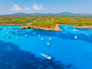 Aerial drone view of yachts and boats in a sea bay in Mallorca, Spain. Summer vacation, leisure and recreation near the Mediterranean coastal forest.