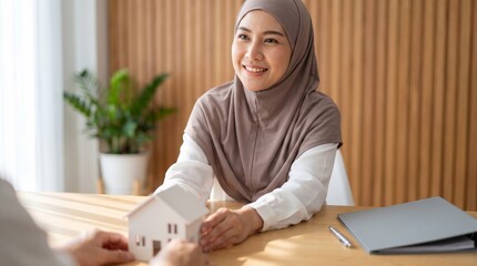 Islamic mortgage advisor in taupe headscarf presenting house model across desk