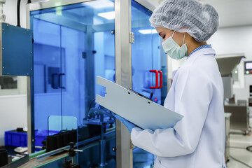 Close up of Asian female scientist checking black plastic bottle packaging machine inside laboratory. concept of pharmaceutical medicine production line quality control.