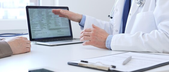 Close-up of a doctor reviewing digital test results with patient, discussing health findings on laptop screen during clinical consultation. Medicine and health care concept