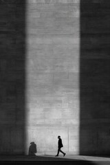 Dramatic shadow play shows a person walking past a textured wall during the day with clear outlines of shadows cast on the surface