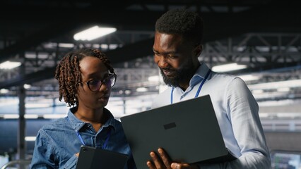 Data center system administrators review AI and LLM visualizations on a laptop while IT specialists analyze neural network outputs and maintain stable equipment operations across the server hub.