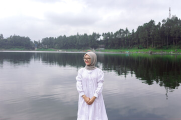 Portrait of a Muslim woman wearing a white hijab on the bank of a river. A young woman meets a summer daylight by the water.