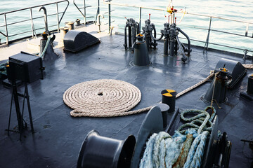 Coiled mooring rope neatly arranged on a steel ship deck beside winches and bollards, nautical equipment bathed in soft light with calm sea visible beyond; industrial, maritime and travel atmosphere.