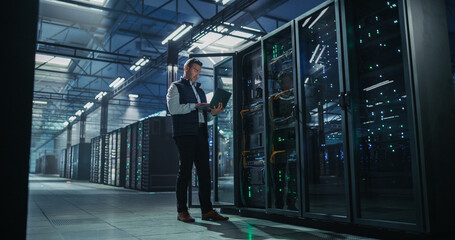 Caucasian Male It Engineer Using Laptop Computer for System Maintenance and Hardware Troubleshooting Beside Open Server Rack Cabinet in Modern Cloud Computing and AI Data Center Warehouse