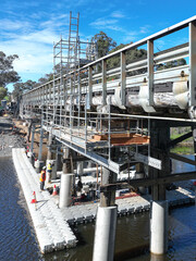 Scaffolding installed on a rural bridge to provide safe access for maintenance and inspection work. Metal platforms and supports surround the bridge structure over a small waterway.