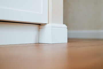 A quarter view shows a white baseboard with a decorative corner piece next to a cabinet.