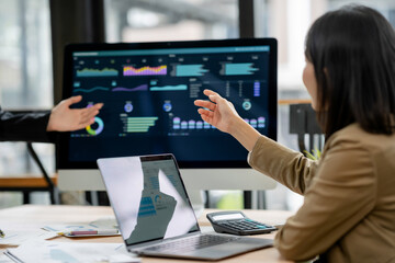 Business people discussing data visualizations on a monitor, analyzing financial charts and reports to develop a strategic plan